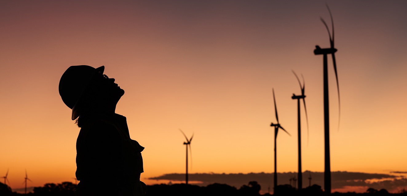 Female worker silhouetted at sunset in foreground of wind turbines